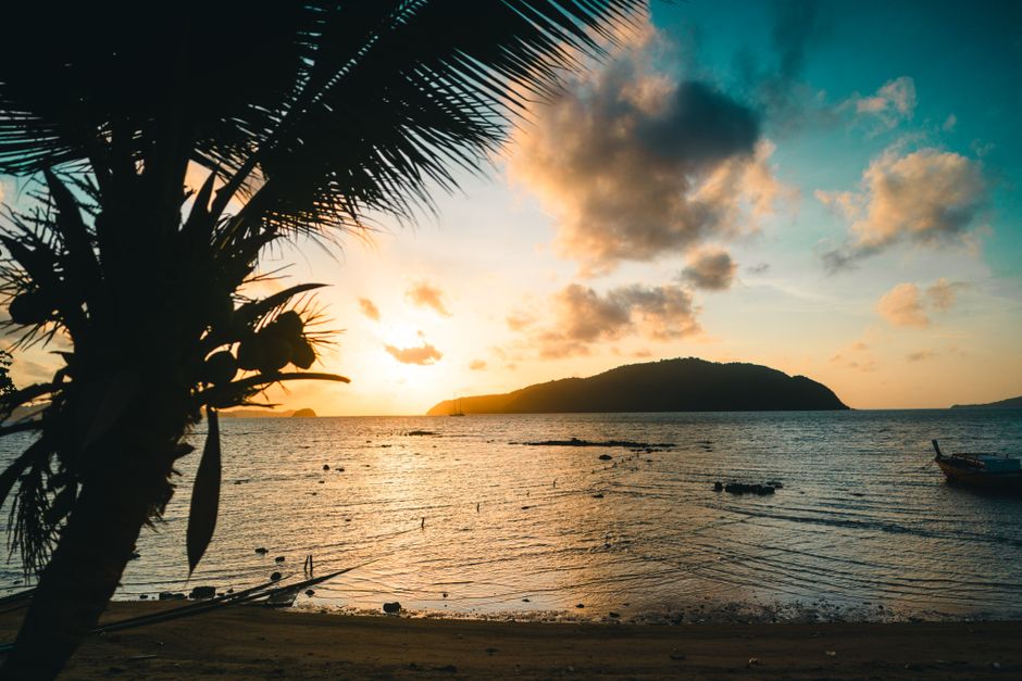 Stunning sunset view over a calm beach in Phuket, Thailand, with silhouetted palm tree and vibrant sky.